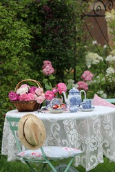 Beautiful roses in wicker basket, porcelain  tea set, fruit on knitted tablecloth, Lovely scene in summer garden, Vintage style, outdoors and space, daylight