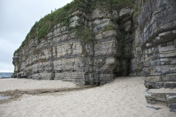 Rocky cliff face with a cave, filled with sand on tropical cliff face and grass, sea side ocean