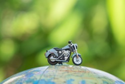 Travel Concept. Close up of miniature motorcycle toy on wolrd balloon map with green nature background.