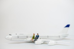 Business and Travel Concept. Businessman and businesswoman miniature figure people sitting on mini airplane model wing on white background.