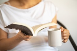 Closeup of woman hand holding and reading a book with holding white mug cup of hot coffee.