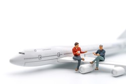 Travel Concept. Two man miniature figure people with cup of coffee sitting and talking on wing of airplane toy model on white background.