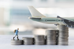 Travel saving and planing concept. Traveler miniature people figure with backpack walking to top of stack of coins with airplane model on top.
