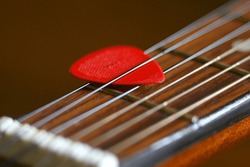 Red guitar pick macro close up. Acoustic guitar. Wooden. Wood. Neck. Strings. Musical instrument. Vintage. Narrow depth of field. Selective focus. Hobby. Entertainment. Play. Song. 