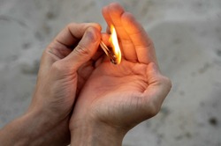 Burning match in hands. The flame from the match pointing to the up. Adult man, sand background.