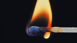 Macro shot of a wooden safety matchstick burning with a bright colorful flame.