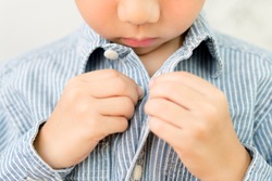 Child Development concept: Close up of a little kindergarten boy's hands learning to get dressed, buttoning his striped blue shirt. Montessori practical life skills - Care of self, Early Education.