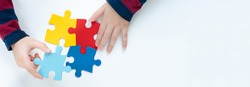 Top view hands of a little child arranging color puzzle symbol of public awareness for autism spectrum disorder. World Autism Awareness Day, ASD, Caring, Speak out, Campaign, Togetherness. Banner.