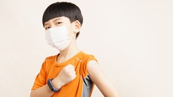 COVID 19 Vaccines for Kids concept. Studio portrait of an adorable asian boy with medical face mask just got his first dose vaccine. Authorized, Approved, Trial, Safe, Available, Back to school.