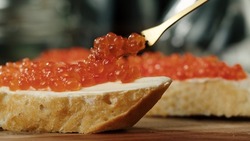 Putting red caviar on bread and butter, close-up of caviar sandwich. Salmon salted orange roe. Raw seafood. Luxury gourmet food. Delicious and tasty fish products. Russian cuisine.