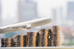 Selective focus of miniature toy airplane over stack of coins with cityscape background, using as background or wallpaper travel concept.