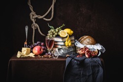 A classic still-life in the Dutch style with fruit cheese and books. On a dark brown background. With draperies
