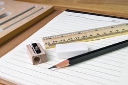 pencil, eraser,ruler with book on woodtable
