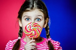 Little girl with big beautiful green eyes holding a big colorful caramel candy.