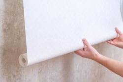 A man rolls out a roll of white wallpaper on the wall with glue. Wallpapering. Repair of a room, apartment, house.