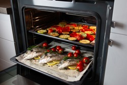 Cooking fish in the oven.Cooking dorado with cherry tomatoes and herbs on parchment in the oven.The supper is ready.We bake sea bass on a grill.Girl cooks fish and takes it out of the stove.World food