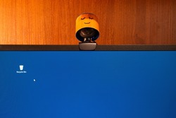 External round black web camera with a smiling cap on a black monitor blue screen. Smiling cover for a webcam. Protection against spying.