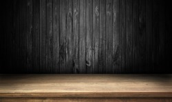 Wooden table on black wall in dark room background. 
