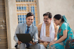 Real estate agent showing online content on laptop to rural Indian family