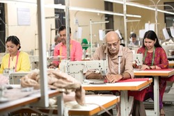 Indian man sewing clothes with sewing machine at textile factory