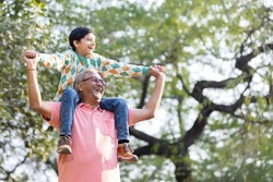Happy grandfather carrying grandson on shoulders at park
