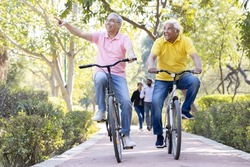 Two cheerful senior men having fun riding bicycle at park
