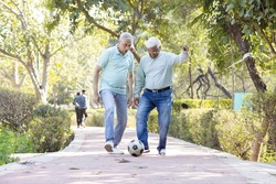 Two senior man having fun while playing football at park
