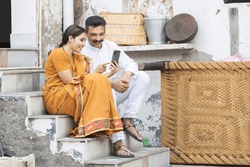 Indian rural woman sitting with husband at home and using smartphone.