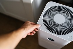 The air purifier turns on the hand of a young fair man. Cleaning and disinfection of the apartment. Modern devices and technologies for comfort.