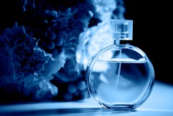 A round bottle of perfume on a dark background, near a bouquet with pink flowers.Aromatherapy and perfumes. Classic blue. The 2020 trend.