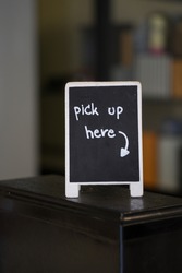 Pick up here sign on black chalk board with arrow symbol pointing. Signs and symbols.