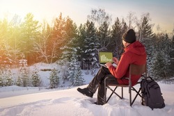 Man working on laptop in forest covered with snow at sunset. Concept remote work.