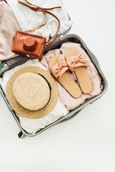Hand luggage with stylish female straw, slippers and retro camera on white background. Flat lay, top view. Summer fashion clothes and travel concept.