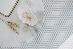 Minimal fashion composition with golden earrings in seashell on marble table with mirror and wheat stalks. Flat lay, top view bijouterie / jewelry concept on mosaic tile background.