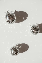 Small shining disco balls with sparkling glitter sunlight shadows on white background. Minimal aesthetic holiday celebration party template layout