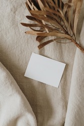 Blank paper sheet card with mockup copy space, dried protea flower on neutral beige linen blanket. Minimal aesthetic business brand template. Flat lay, top view