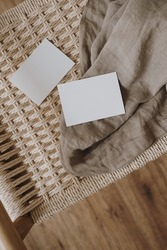 Blank paper sheet card with mockup copy space, grey linen cloth on neutral beige rattan bench. Minimal aesthetic business brand template. Flat lay, top view