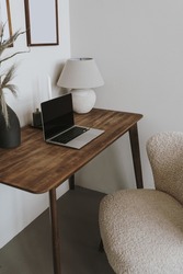 Laptop computer on table with lamp and comfortable chair. Aesthetic home office workspace interior design. Online shopping, online store, social media, blog branding