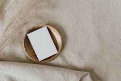Flatlay of blank paper card on brass dish, pampas grass on neutral beige crumpled linen cloth. Business template. Top view, flat lay minimalist aesthetic luxury bohemian business branding concept