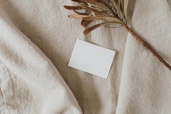 Aesthetic luxury bohemian branding or invitation card template. Blank paper, invitation card sheet with empty mock up copy space, dried protea flower on neutral beige crumpled linen cloth