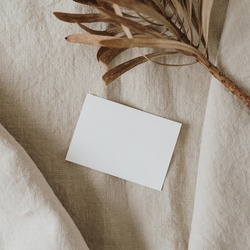 Flatlay of blank paper card, dried protea flower on neutral beige crumpled linen cloth. Business template. Top view, flat lay minimalist aesthetic luxury bohemian business branding concept