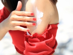 Woman hand with red cloth and healthy skin applying sunscreen to shoulder which she is  protection of sunburn and cancer prevention concept.