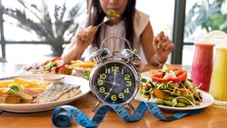 Selective focus of Alarm clock with woman eating a healthy food as Intermittent fasting, time-restricted eating
