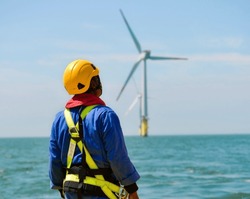 Man and standing at an offshore and wind turbine.