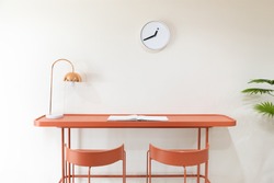 front view of orange study desk or workplace with metal electrical table lamp and white minimalist clock without numbers hanging on the wall