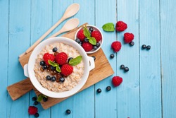 Porridge with fresh berries on blue wooden background. Healthy breakfast, health and diet concept.