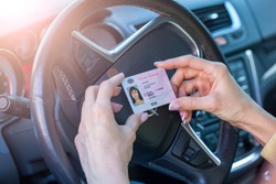 Getting a driver's license, female hands show US driving license, amid the steering wheel of a car