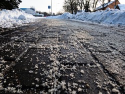 Salt grains on icy sidewalk surface in the winter. Applying salt to keep roads clear and people safe in winter weather from ice or snow, closeup view.