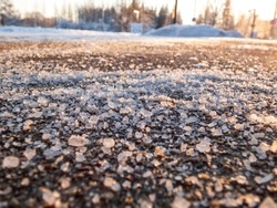 Salt grains on icy sidewalk surface in the winter. Applying salt to keep road clear and people safe in winter weather from ice or snow. Macro view of salt grains in sunlight in winter