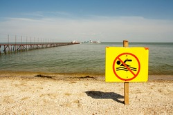 sign no swimming on the background of the sea and pier, a sign on a yellow background
